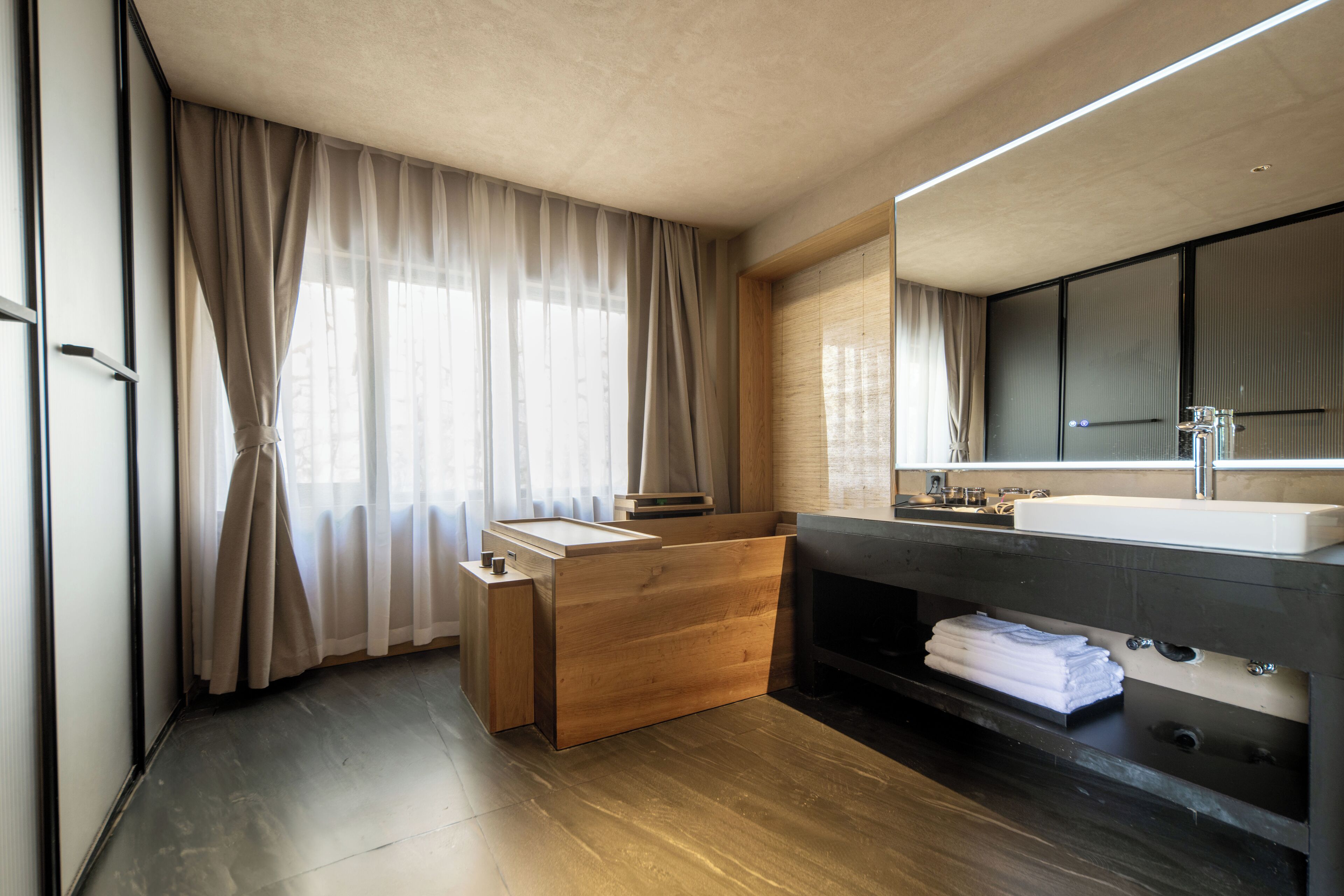 Un baño moderno con tocador de madera, un lavamanos grande y una zona de ducha integrada.