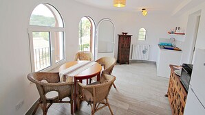 A dining area with a wooden table and wicker chairs, large windows, and a kitchen with a microwave.