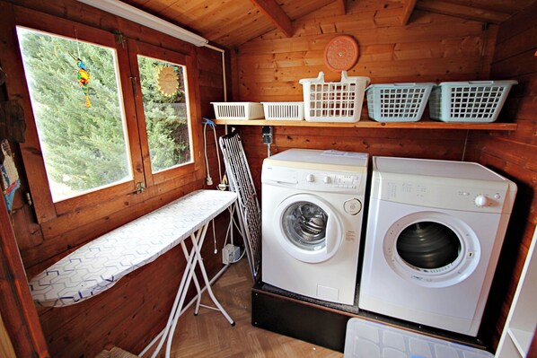 A laundry room with two washing machines, a drying rack, and a shelf with laundry baskets.