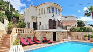 A poolside area with a pool, sun loungers, and a building with a stone facade and balconies.