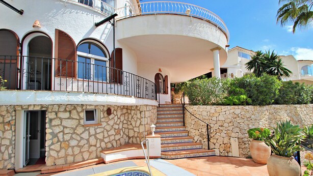 A pool area with a stone wall, a staircase, and a balcony with a railing.