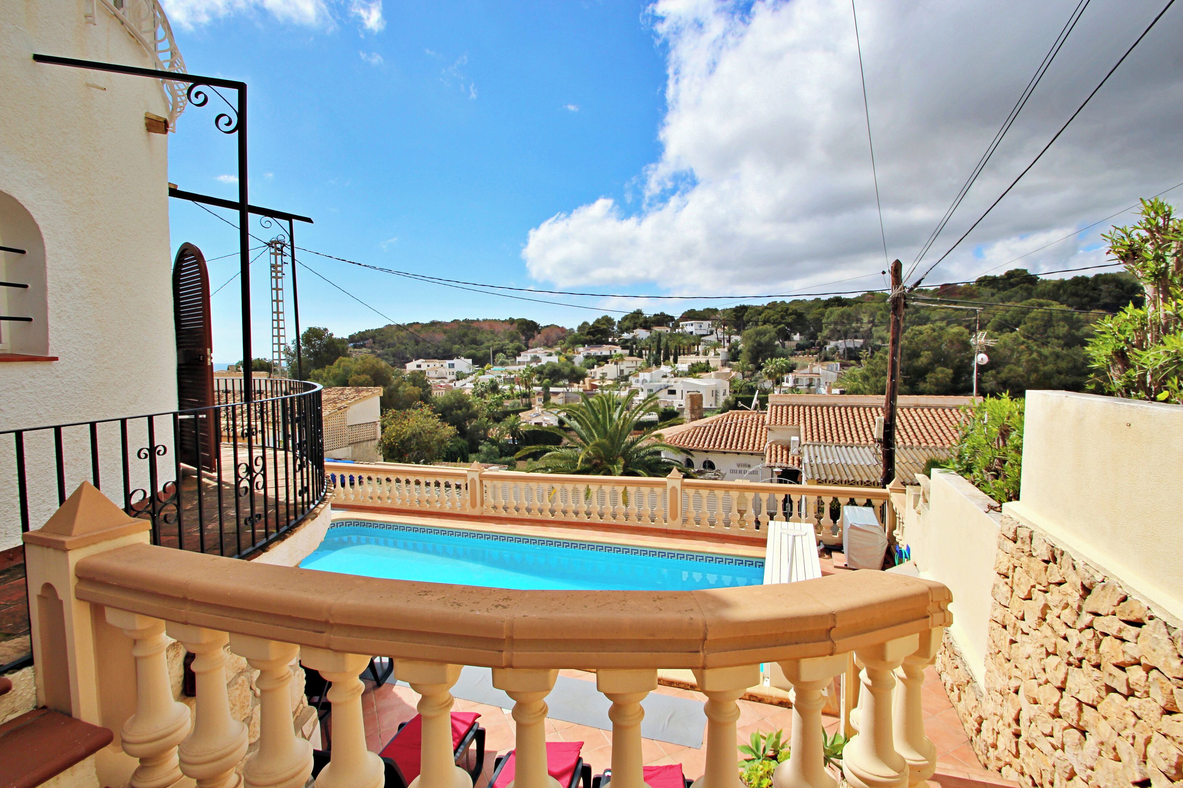 Un espace piscine offrant une vue sur une ville perchée sur une colline, un balcon avec une balustrade et un mur en pierre.