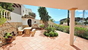 A patio with outdoor furniture, a stone wall, and a view of the sea.