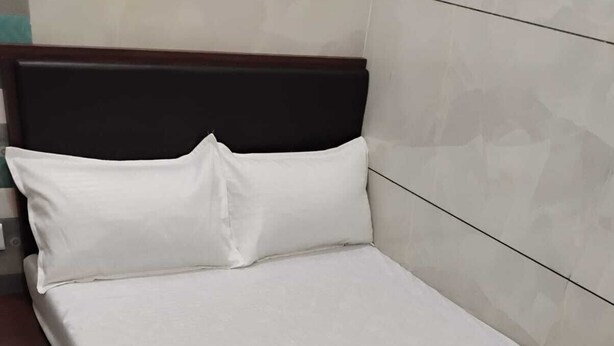 Una cama individual con cabecera de madera y ropa de cama blanca en una habitación con paredes de baldosas.