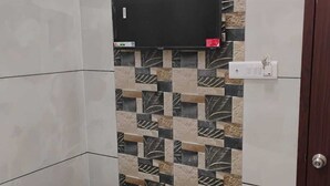 Un baño con pared de azulejos, televisor montado y una puerta.