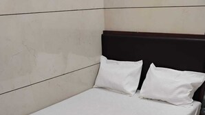 Una cama individual con colchón blanco y dos almohadas, cabecera de madera y suelo de baldosas.