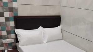 Una cama individual con ropa de cama blanca en una habitación con pared de azulejos y una mesita de noche de madera.