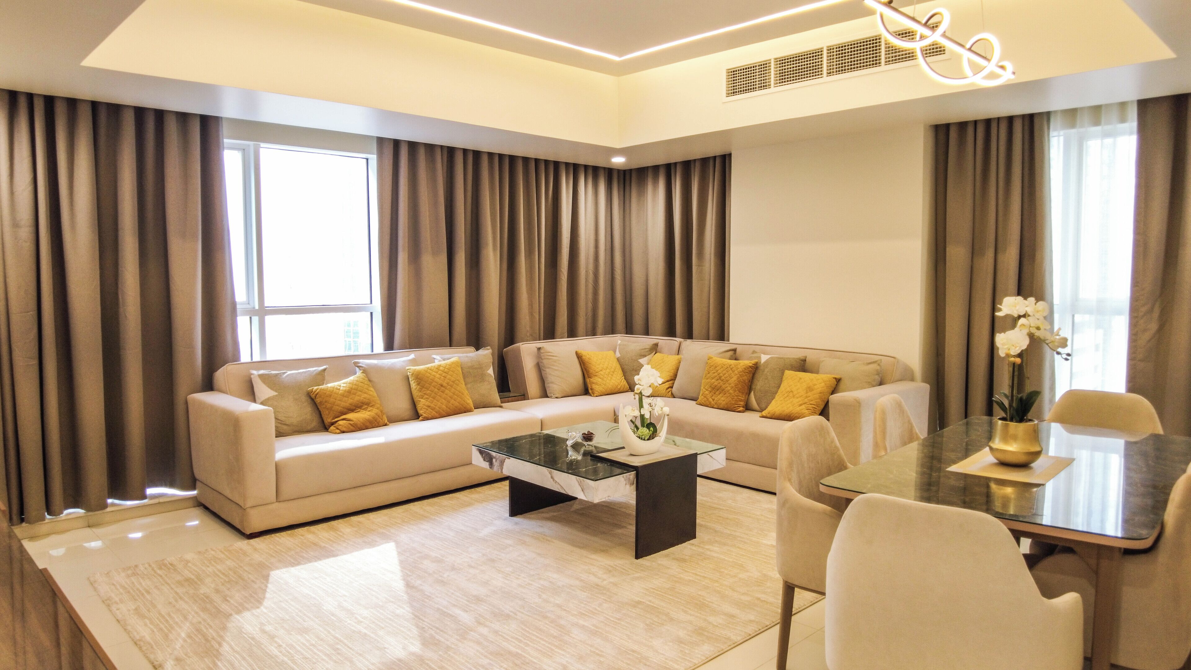A modern living room with a beige sofa, a glass coffee table, and a dining table with chairs.