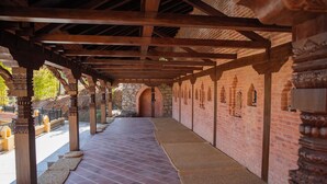 A covered walkway with wooden beams and brick walls, featuring a tiled floor and decorative columns. - Jungle Mahal Wellness Resort (Chandragiri)