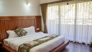 A large bed with a wooden headboard, white bedding, and a green decorative pillow. - Jungle Mahal Wellness Resort (Chandragiri)