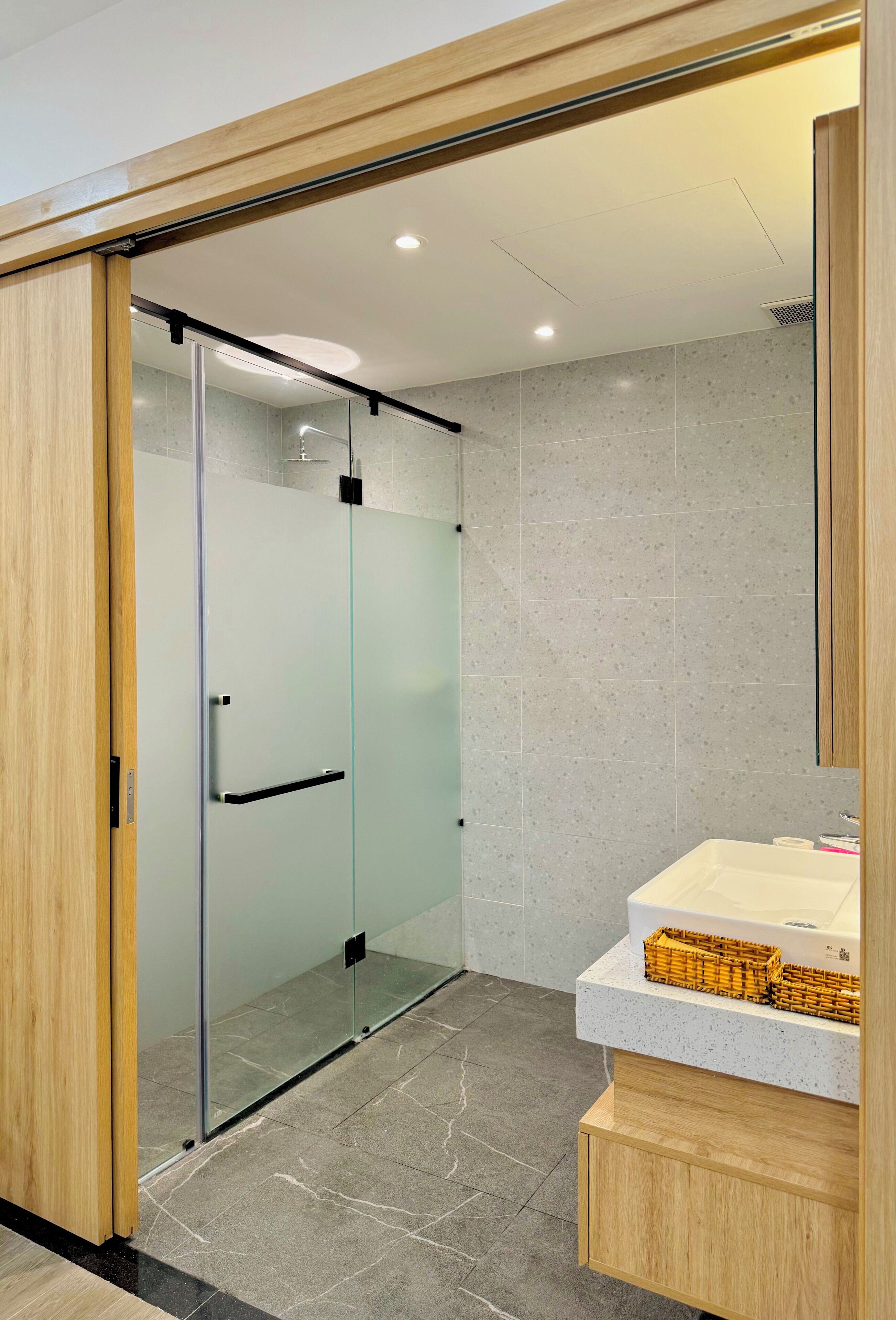 A modern bathroom with a glass shower enclosure, a wooden vanity, and a tiled floor.