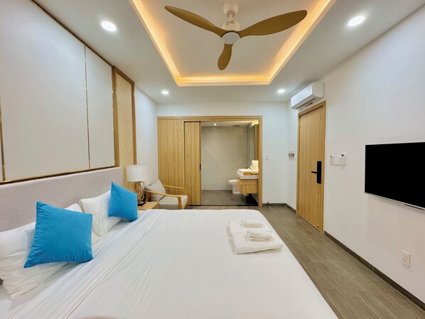 A hotel room with a large bed, a ceiling fan, a TV, and a bathroom visible through an open door. - Hai Bot Home 16 (Phu Quoc)