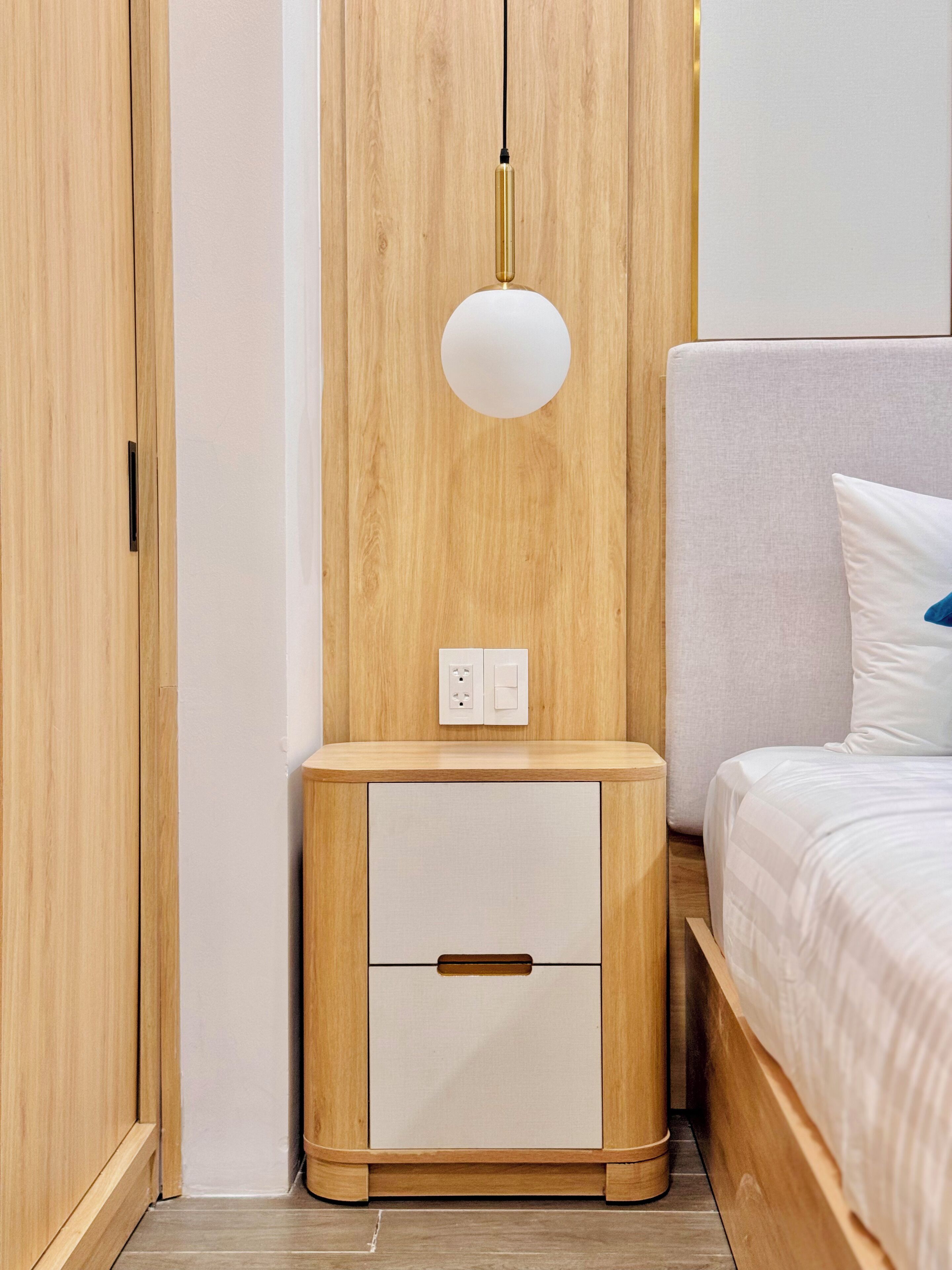 Un dormitorio con un armario de madera, una mesita de noche con lámpara y una cama con almohada.