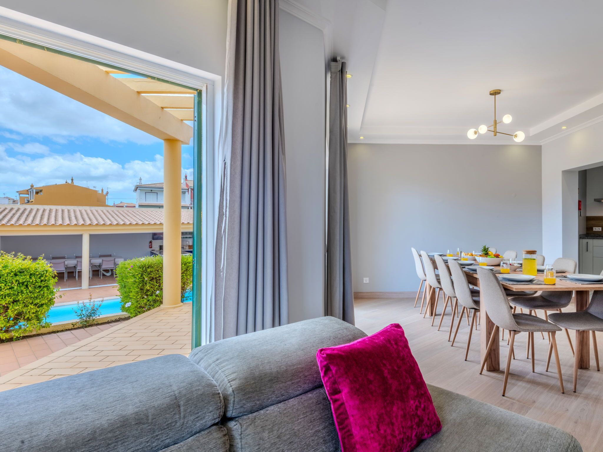A modern living room with a grey sofa, a vibrant pink pillow, and a dining area with a table set for four.