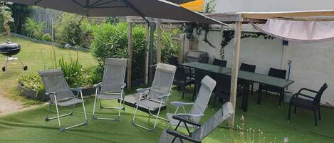An outdoor patio with a grill, chairs, and a table under a canopy.