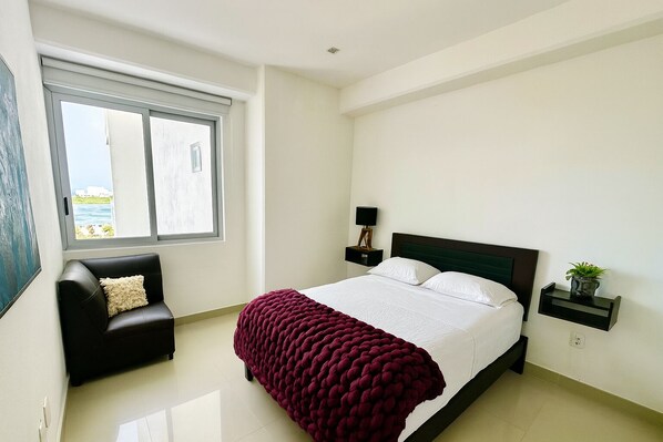 A bedroom with a bed, a chair, a nightstand, and a window with a view.