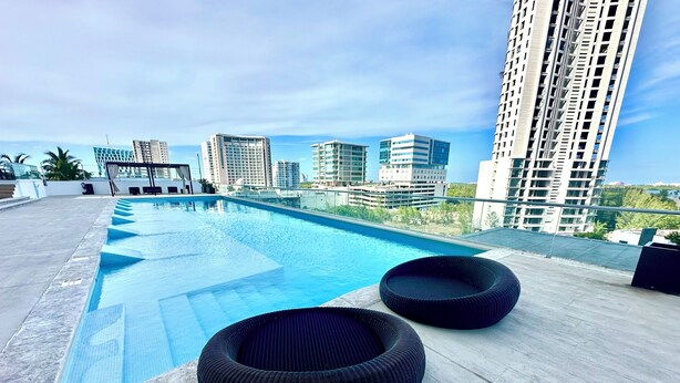 A rooftop pool with two black lounge chairs and a view of modern high-rise buildings. - Cozy 2-bedroom apartment in beautiful Cancún with WiFi, AC (Cancún)