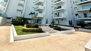 A modern high-rise building with multiple balconies, a landscaped courtyard, and a clear sky. - Cozy 2-bedroom apartment in beautiful Cancún with WiFi, AC (Cancún)