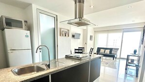A modern kitchen with a built-in island, stainless steel appliances, and a large window providing natural light. - Cozy 2-bedroom apartment in beautiful Cancún with WiFi, AC (Cancún)