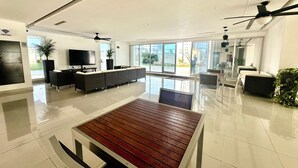 A modern, spacious living area with a large wooden table, comfortable seating, a flat-screen TV, and large windows offering views of the outdoors. - Cozy 2-bedroom apartment in beautiful Cancún with WiFi, AC (Cancún)
