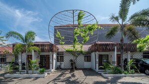 A courtyard with a central circular structure, surrounded by buildings with wooden balconies and palm trees. - Senyum Bali inn (Denpasar)