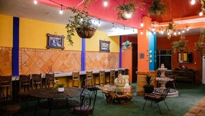 A restaurant with multiple tables and chairs, hanging plants, and a tiled wall with geometric patterns. - Casa Márquez (Leon)
