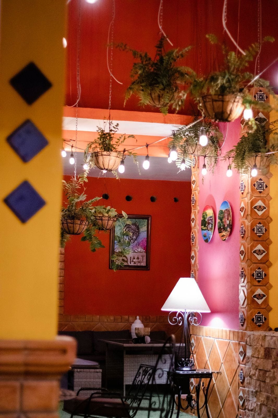 A cozy interior with hanging plants, string lights, and a tiled wall with decorative patterns.