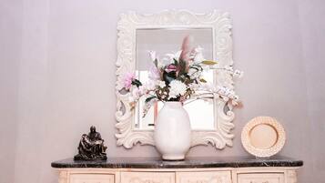 A vanity with a mirror, a vase of flowers, a statue, and a decorative plate.
