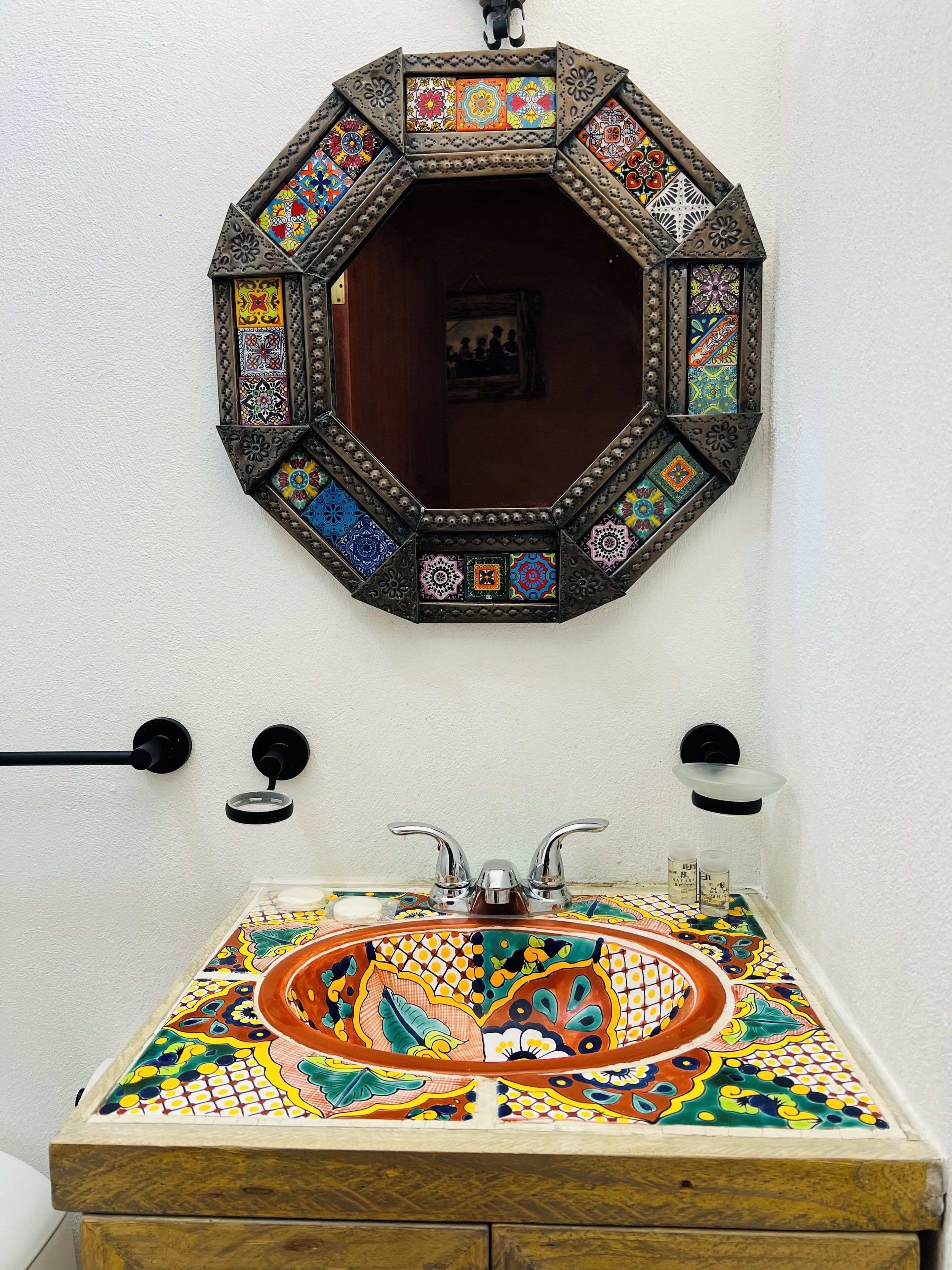 A bathroom with a colorful mosaic sink and a decorative octagonal mirror.