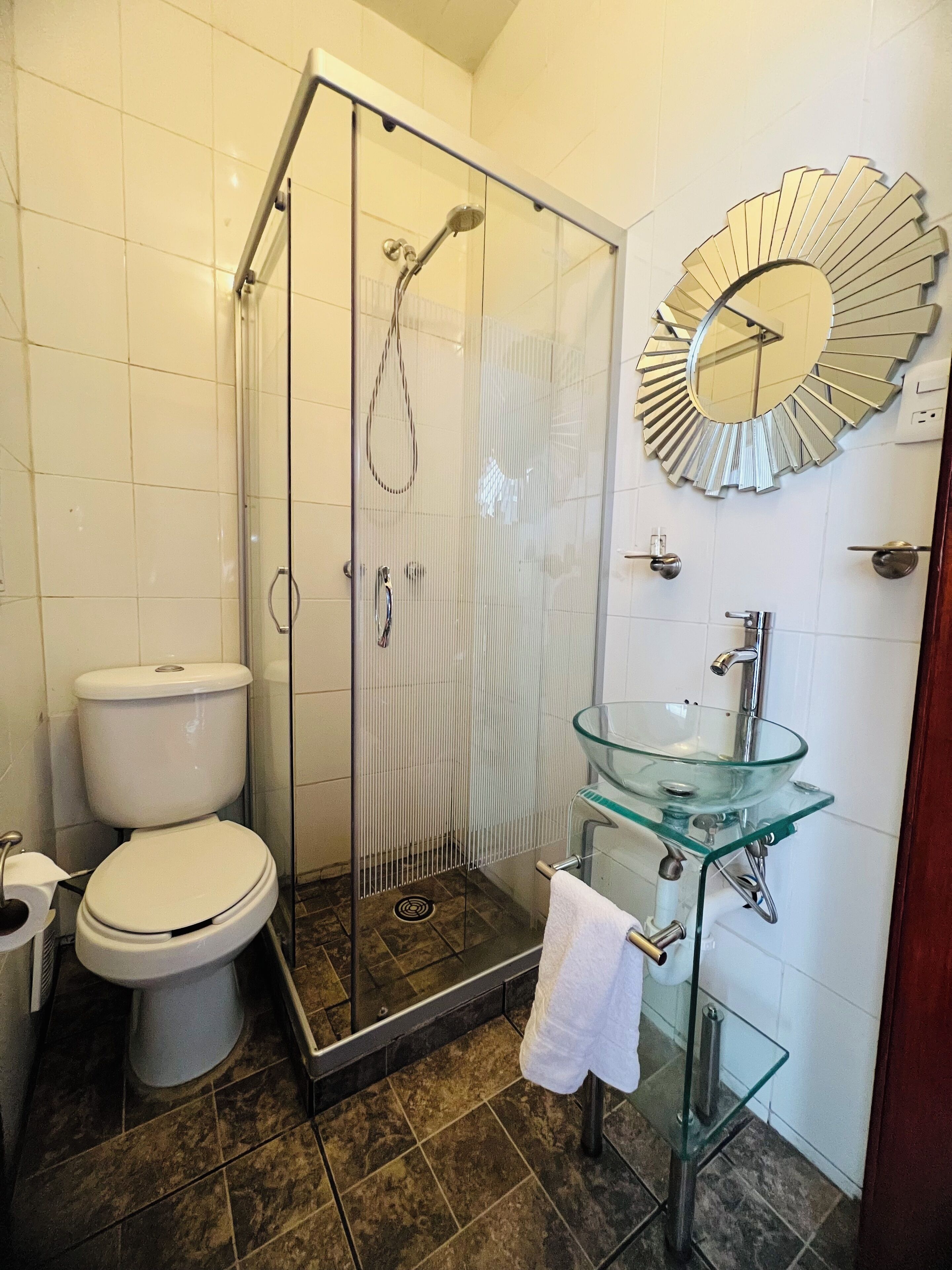 Un baño con ducha acristalada, lavamanos de vidrio y un inodoro.