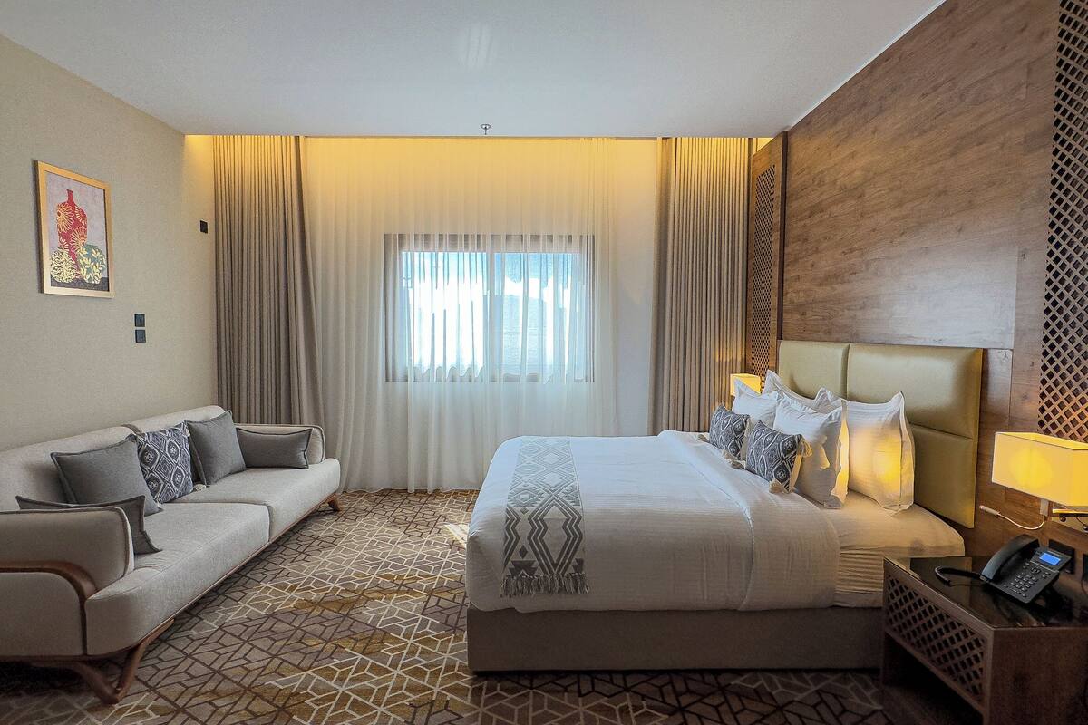 A hotel room with a bed, a sofa, a bedside table with a lamp, and a patterned floor.