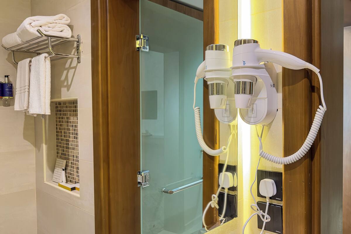 A bathroom with a towel rack, a glass shower enclosure, and hair dryers mounted on the wall.
