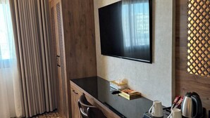 Een hotelkamer met een flatscreen televisie aan de muur, een houten bureau met een stoel, een dienblad met kopjes en een waterkoker, en een vloer met een patroon.