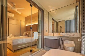A modern hotel room with a large bed, a separate bathroom, a glass shower enclosure, and a marble-topped vanity.