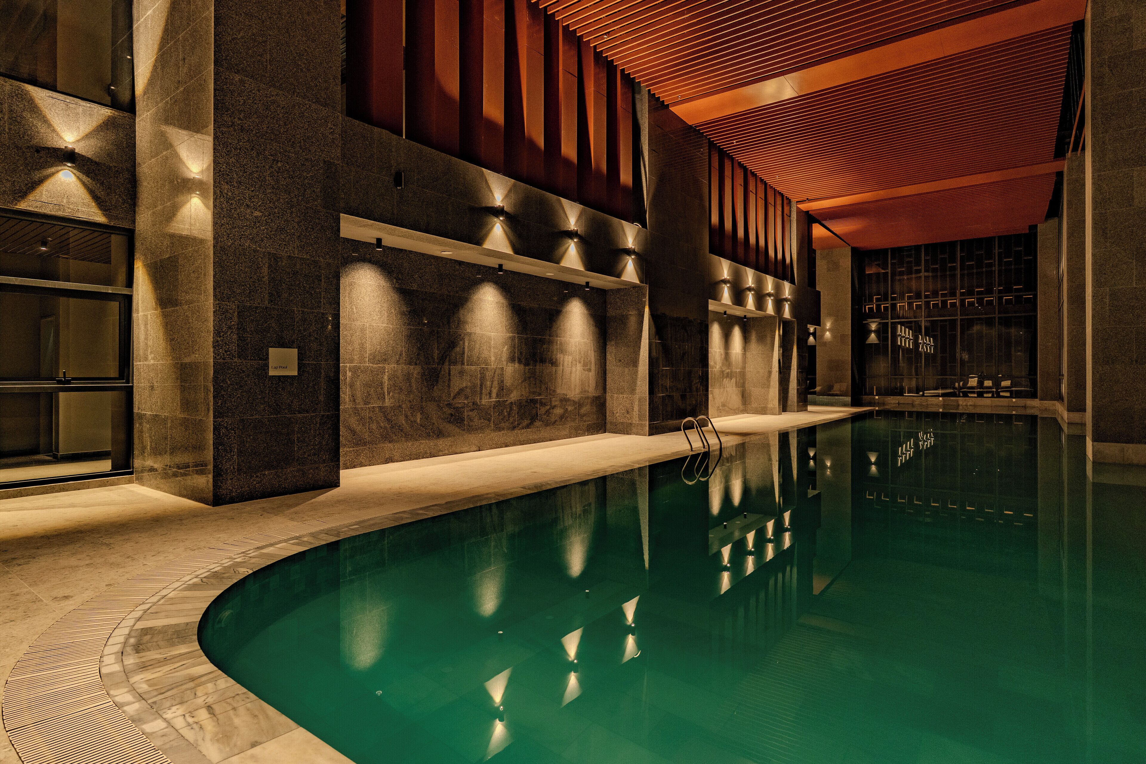An indoor swimming pool with a curved design, surrounded by stone walls and wooden paneling.