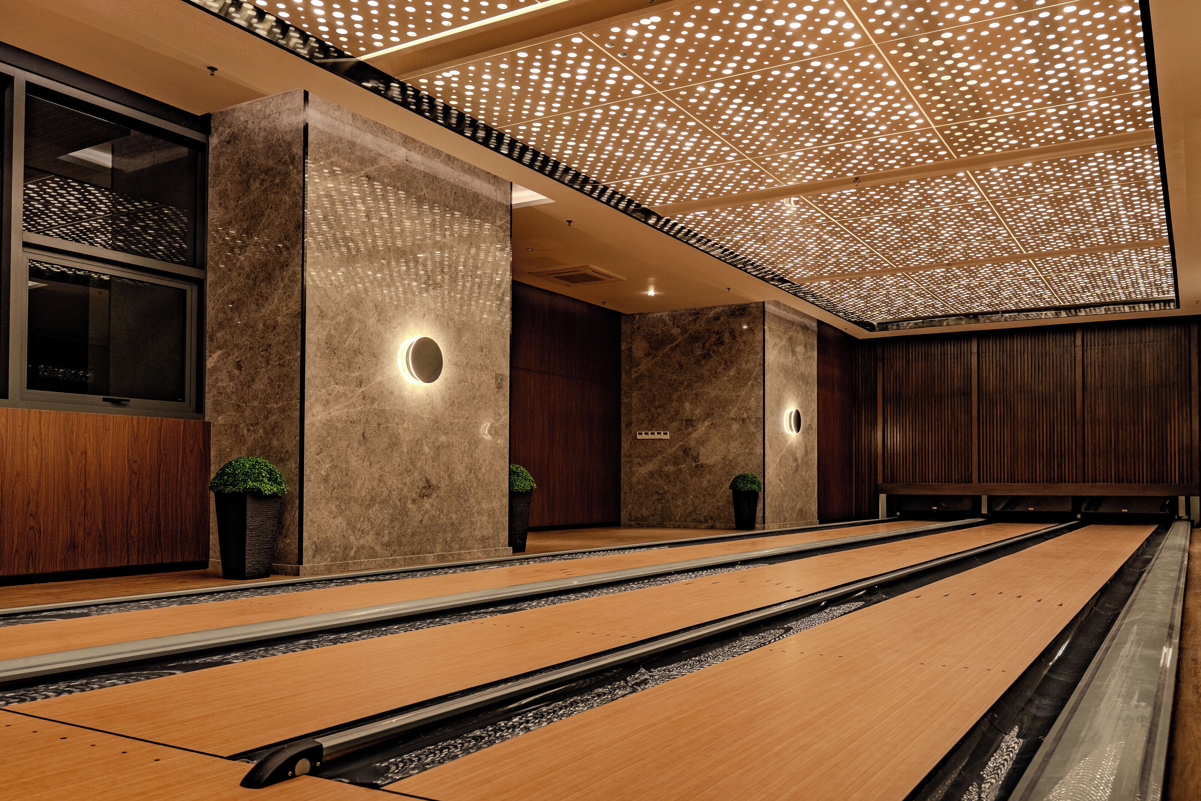 A modern bowling alley with wooden lanes and a ceiling with a perforated design.