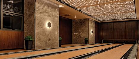 A modern bowling alley with wooden lanes and a ceiling with a perforated design.