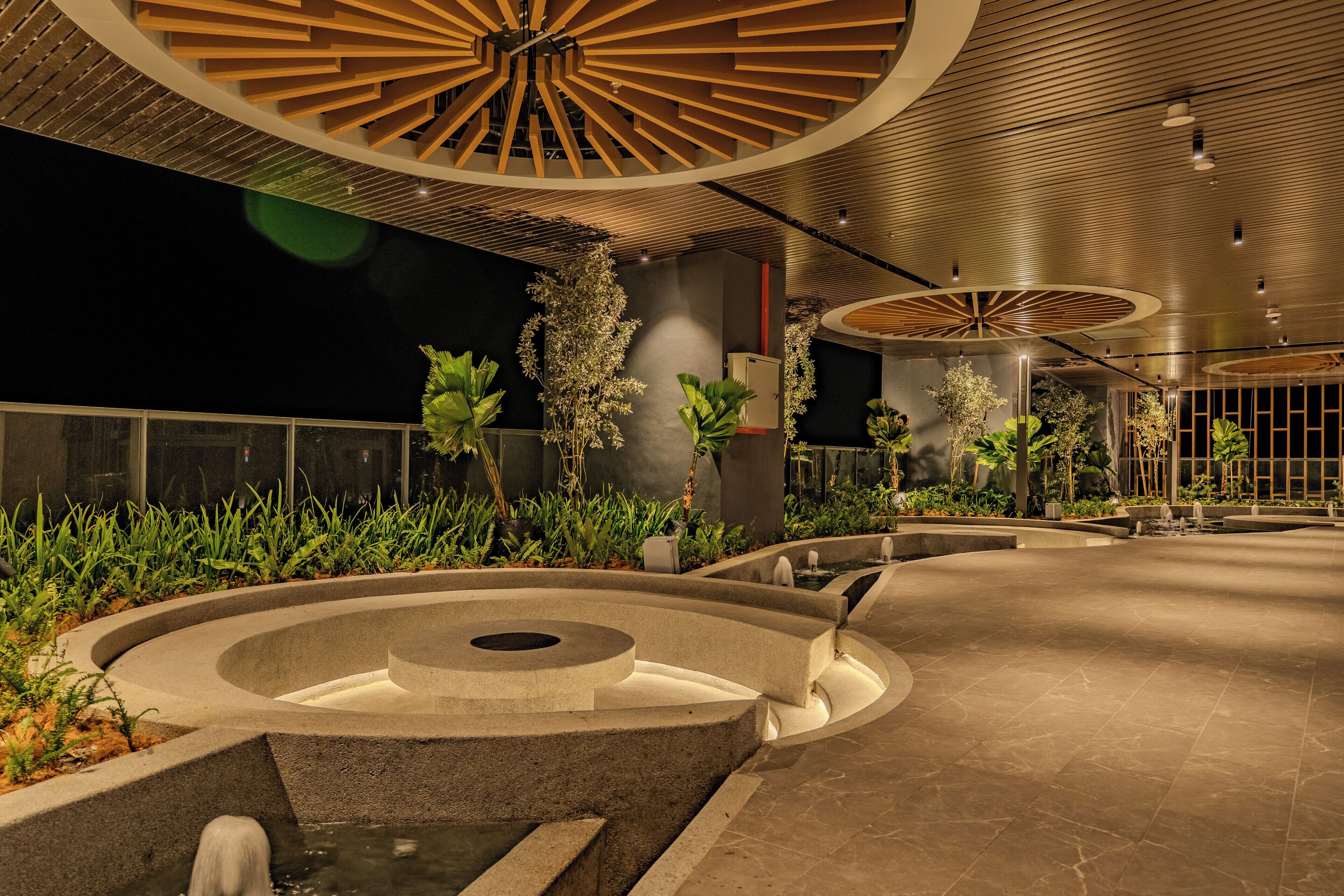 Un patio interior moderno con una fuente central, rodeado de macetas y una zona de estar circular.