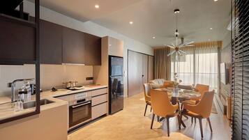 A modern kitchen with a built-in oven, a refrigerator, and a dining area with a round table and orange chairs.