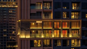 A modern building with multiple balconies and windows, featuring a glass railing and warm interior lighting.