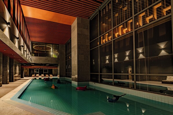 A modern indoor swimming pool with geometric lighting and a high ceiling.