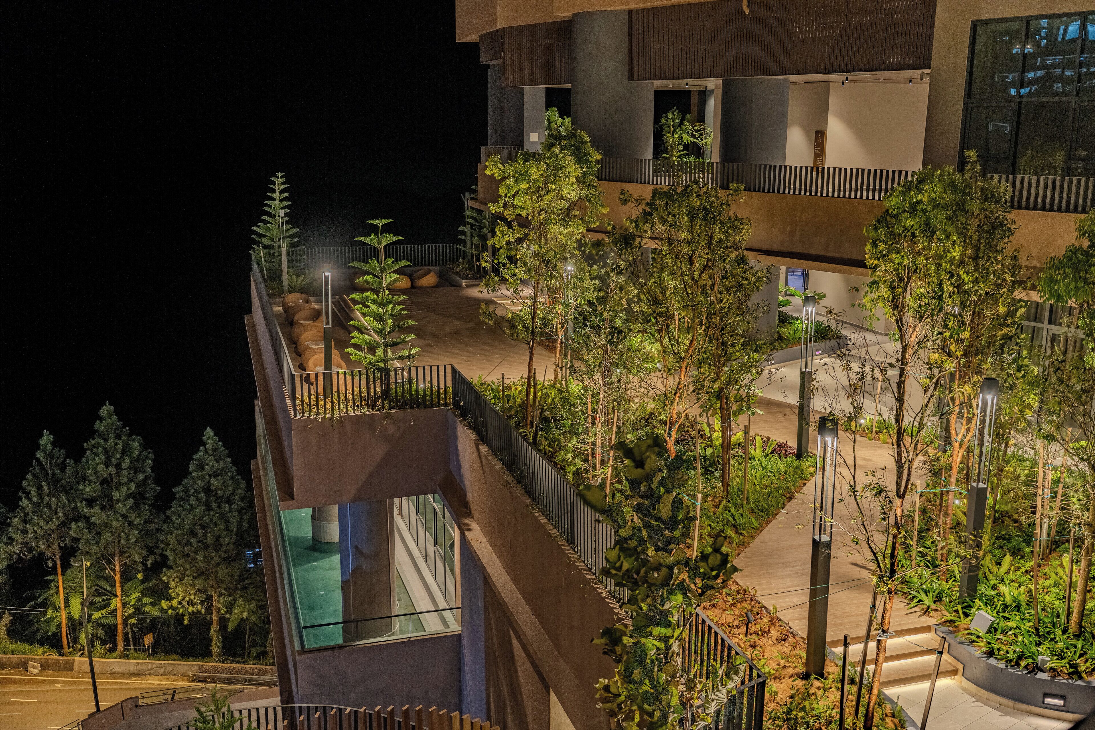 A multi-story building with a modern architectural design, featuring balconies, glass railings, and a landscaped garden area.