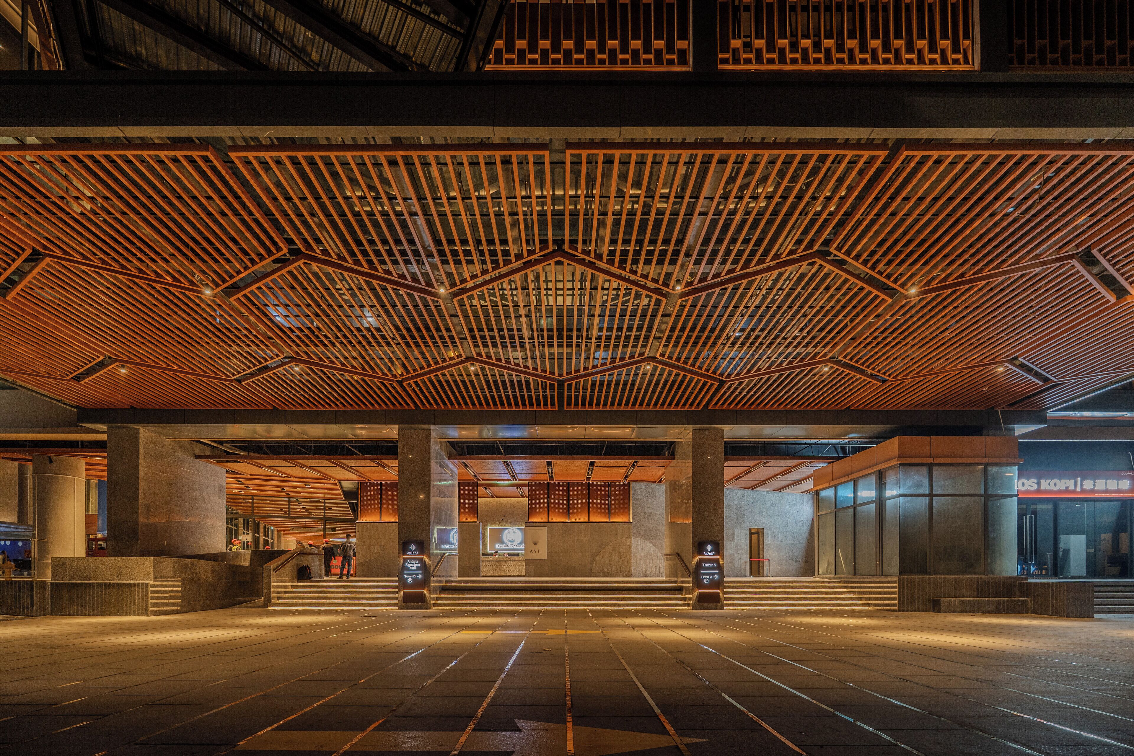 Un lobby espacioso con un diseño geométrico en el techo, columnas grandes y un mostrador de recepción moderno.