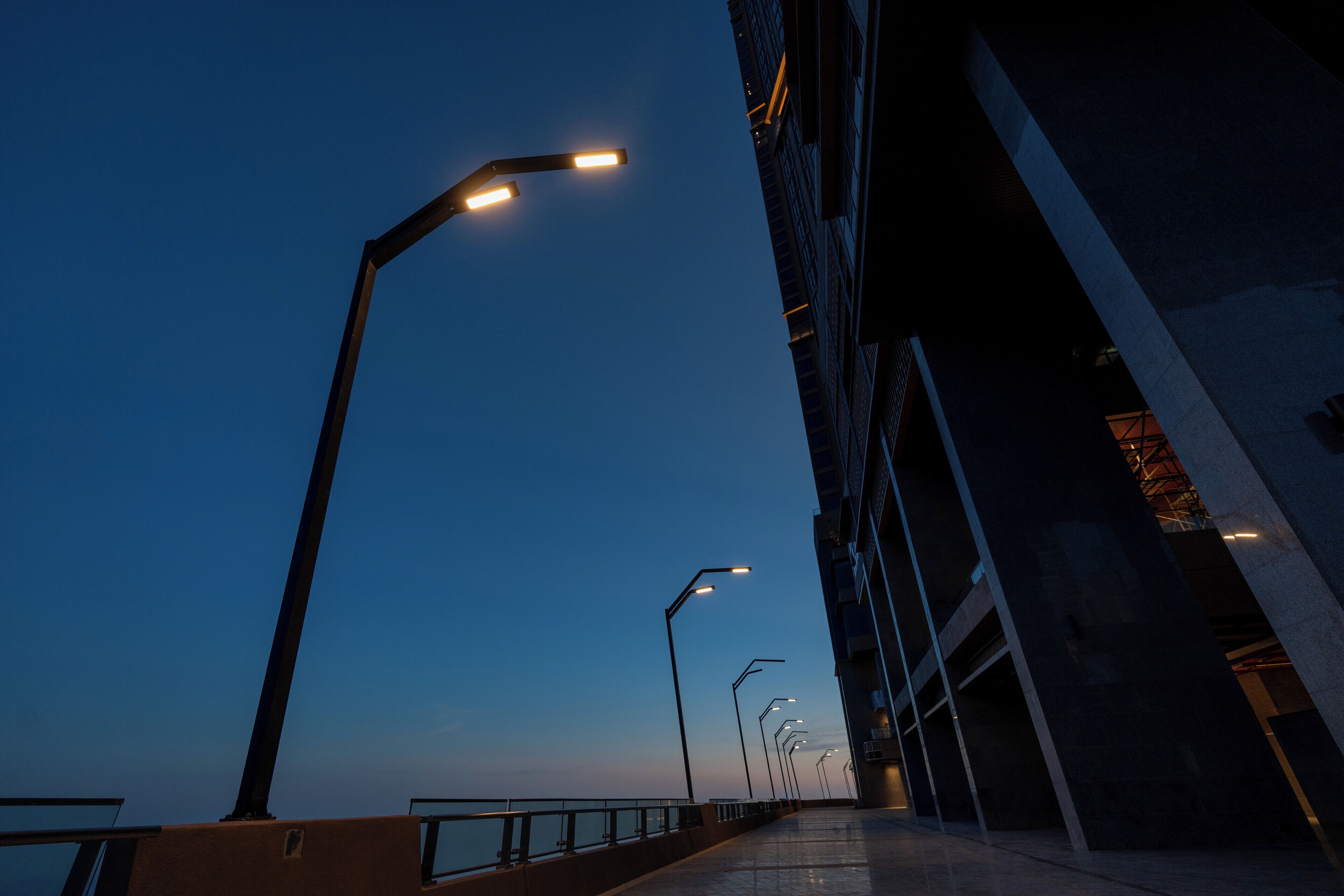 A long, empty pedestrian walkway with street lamps and a building on one side.