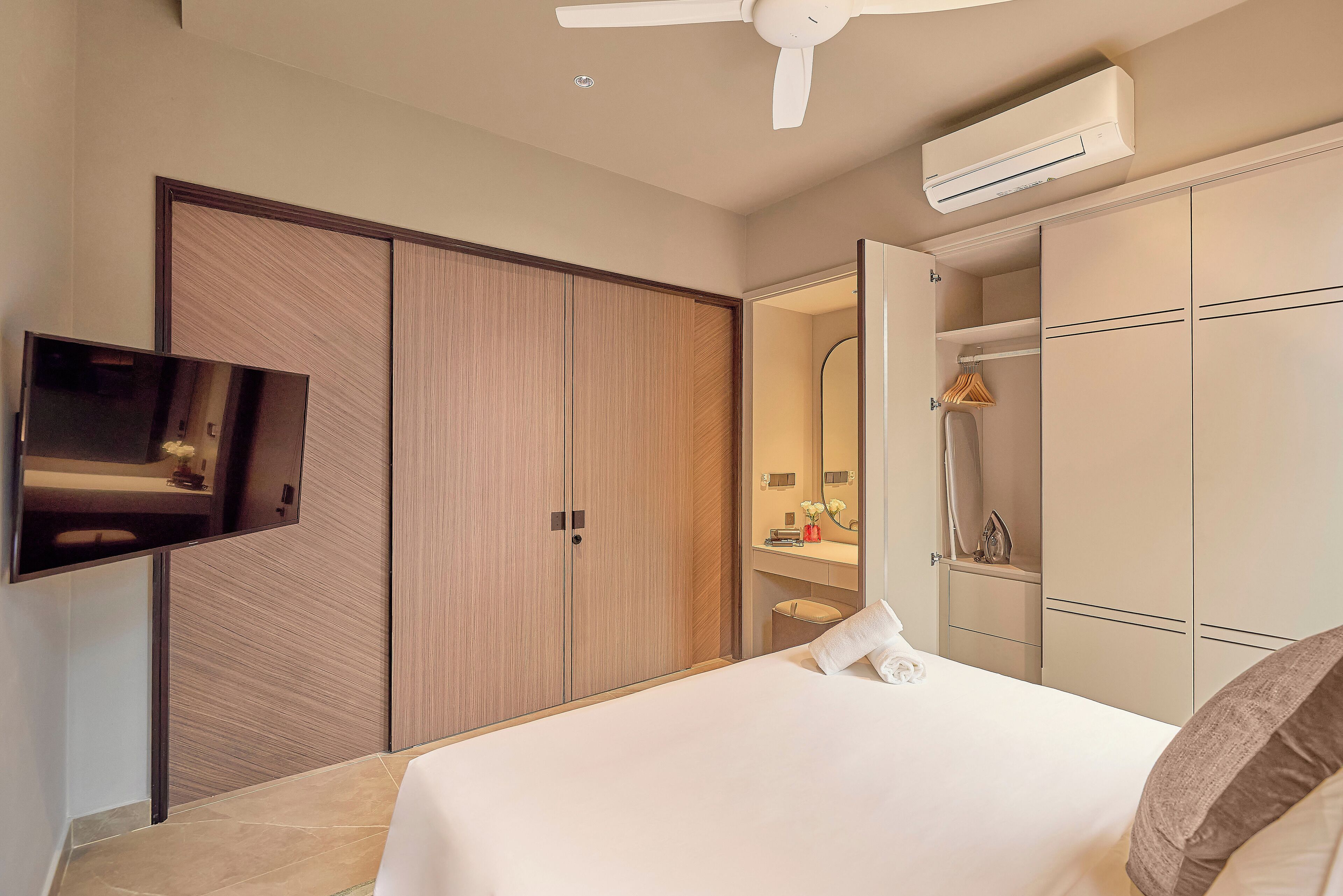 A hotel room with a bed, a TV mounted on the wall, a wardrobe, and a ceiling fan.