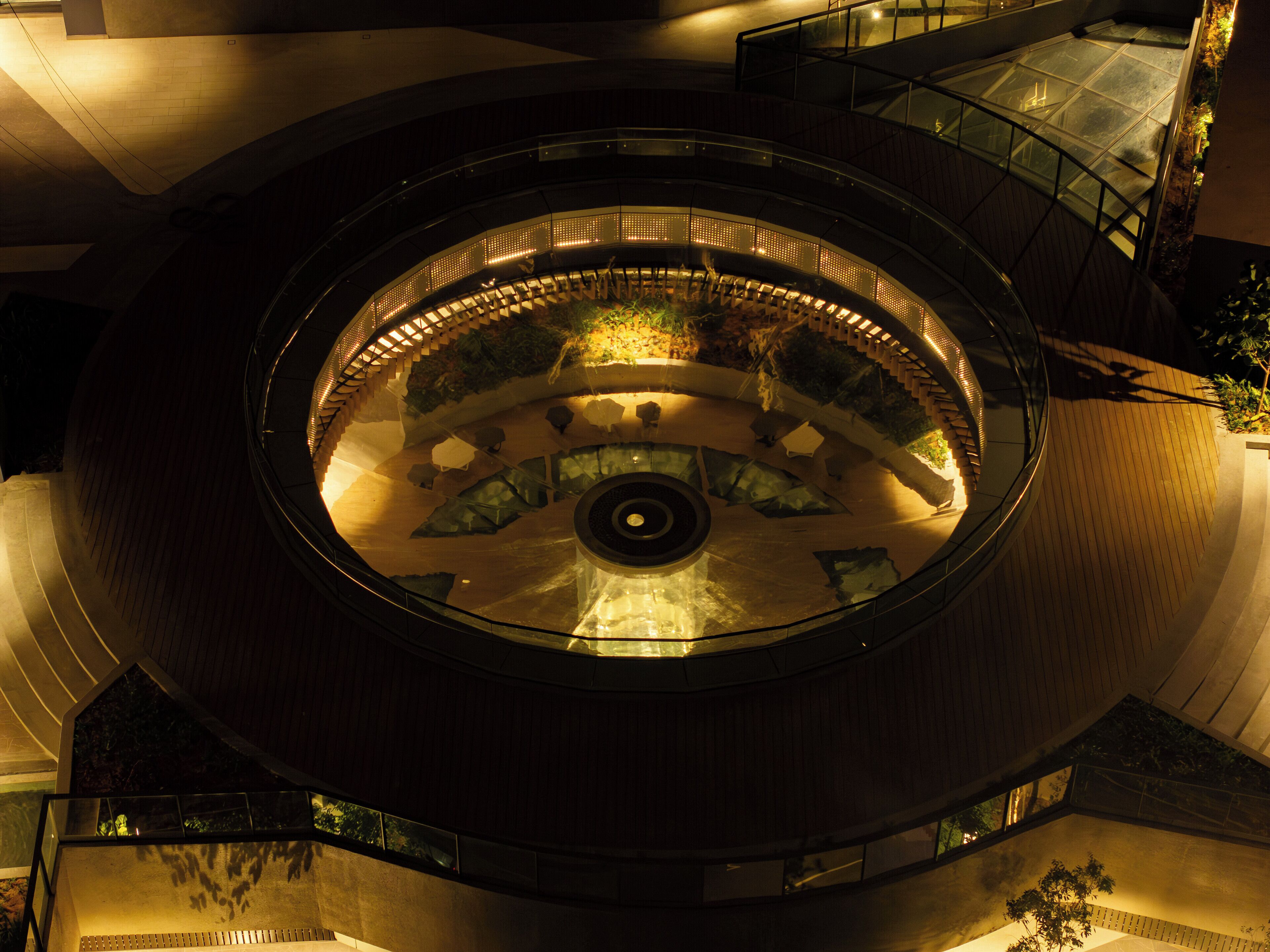 A circular atrium with a central fountain, glass railings, and a wooden floor.