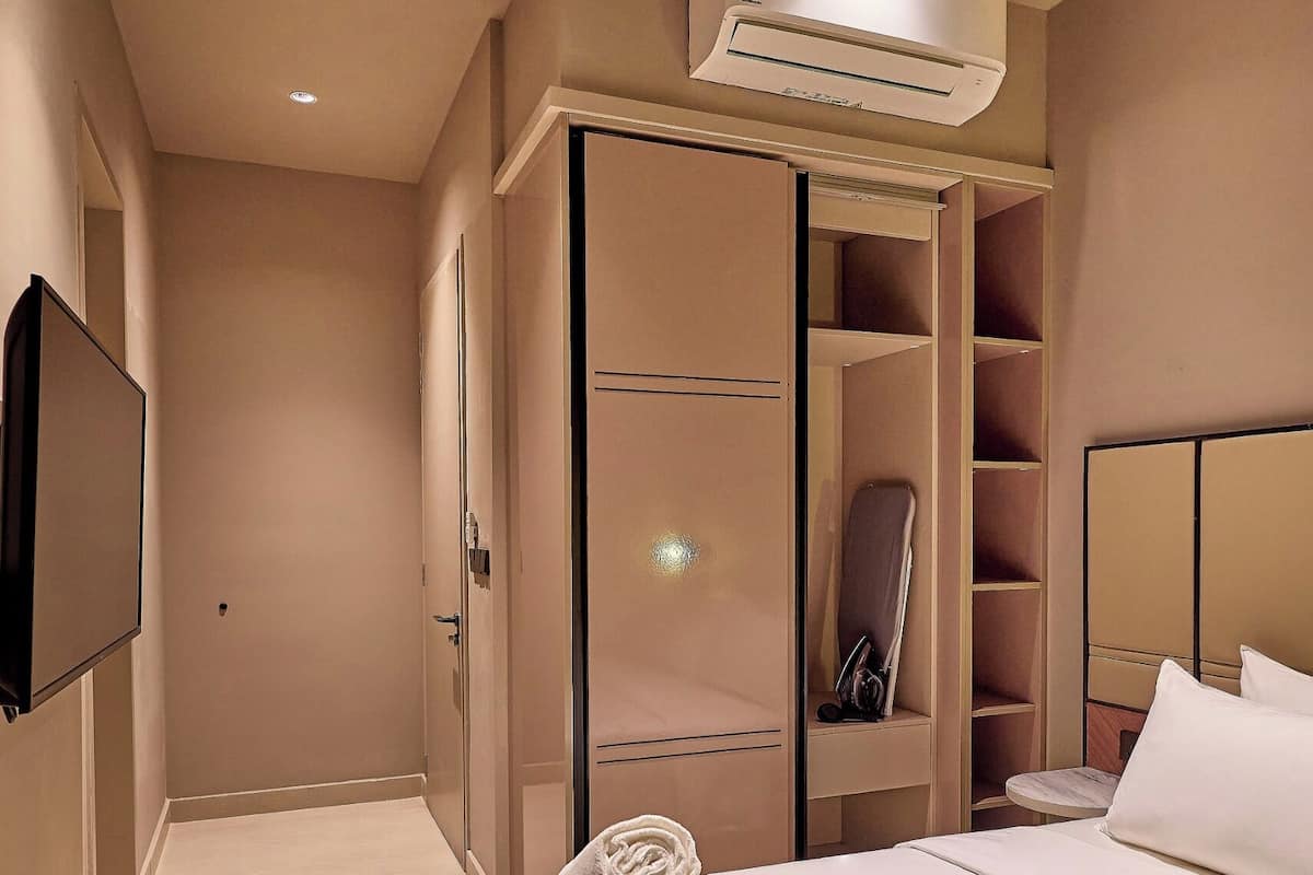 Una habitación de hotel con cama, televisión, aire acondicionado, armario y espejo.