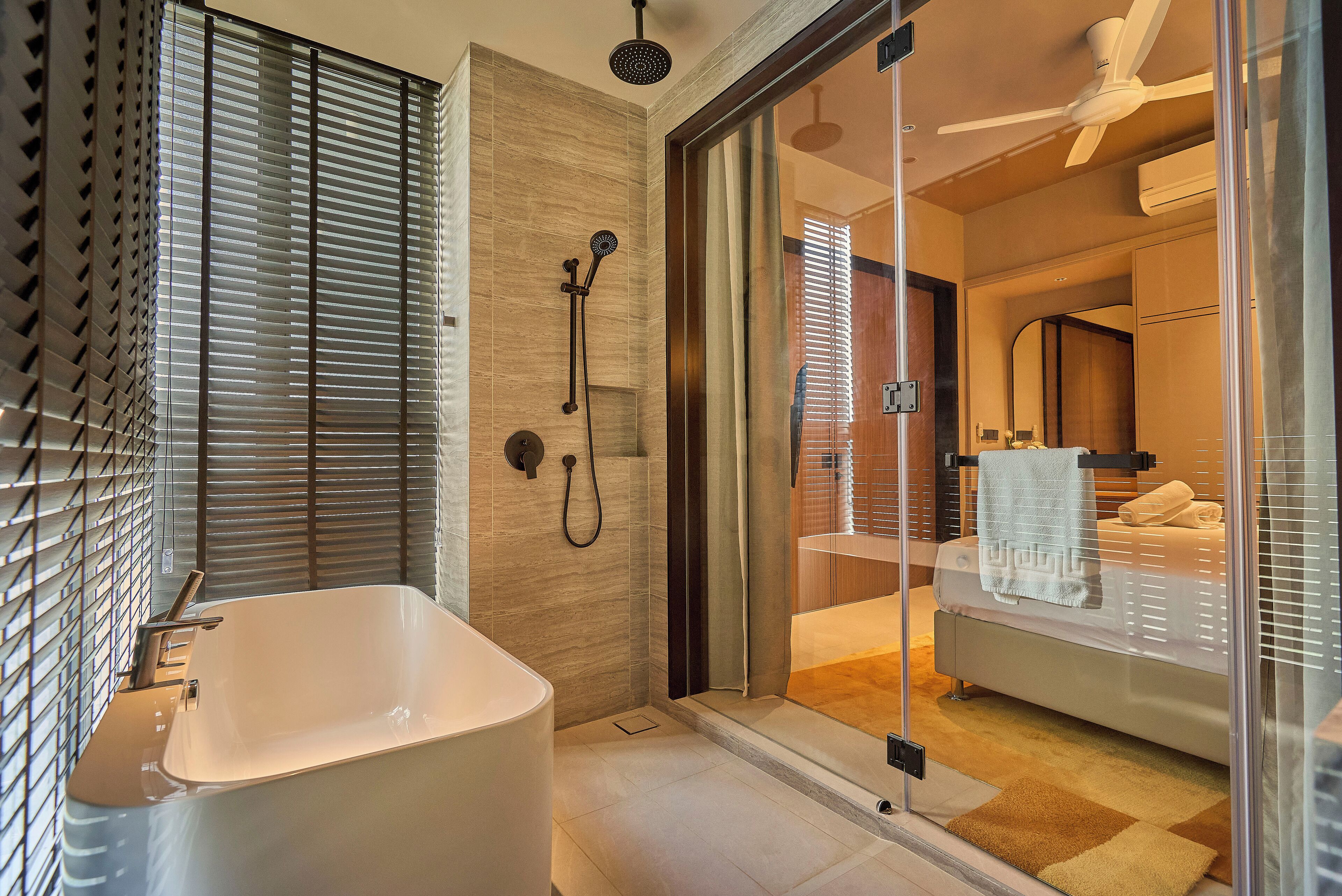 A modern bathroom with a freestanding bathtub, a glass shower enclosure, and a visible bedroom with a bed and a towel.