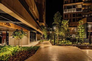 Vista nocturna de un edificio moderno con un camino central, rodeado de vegetación e iluminado por farolas.