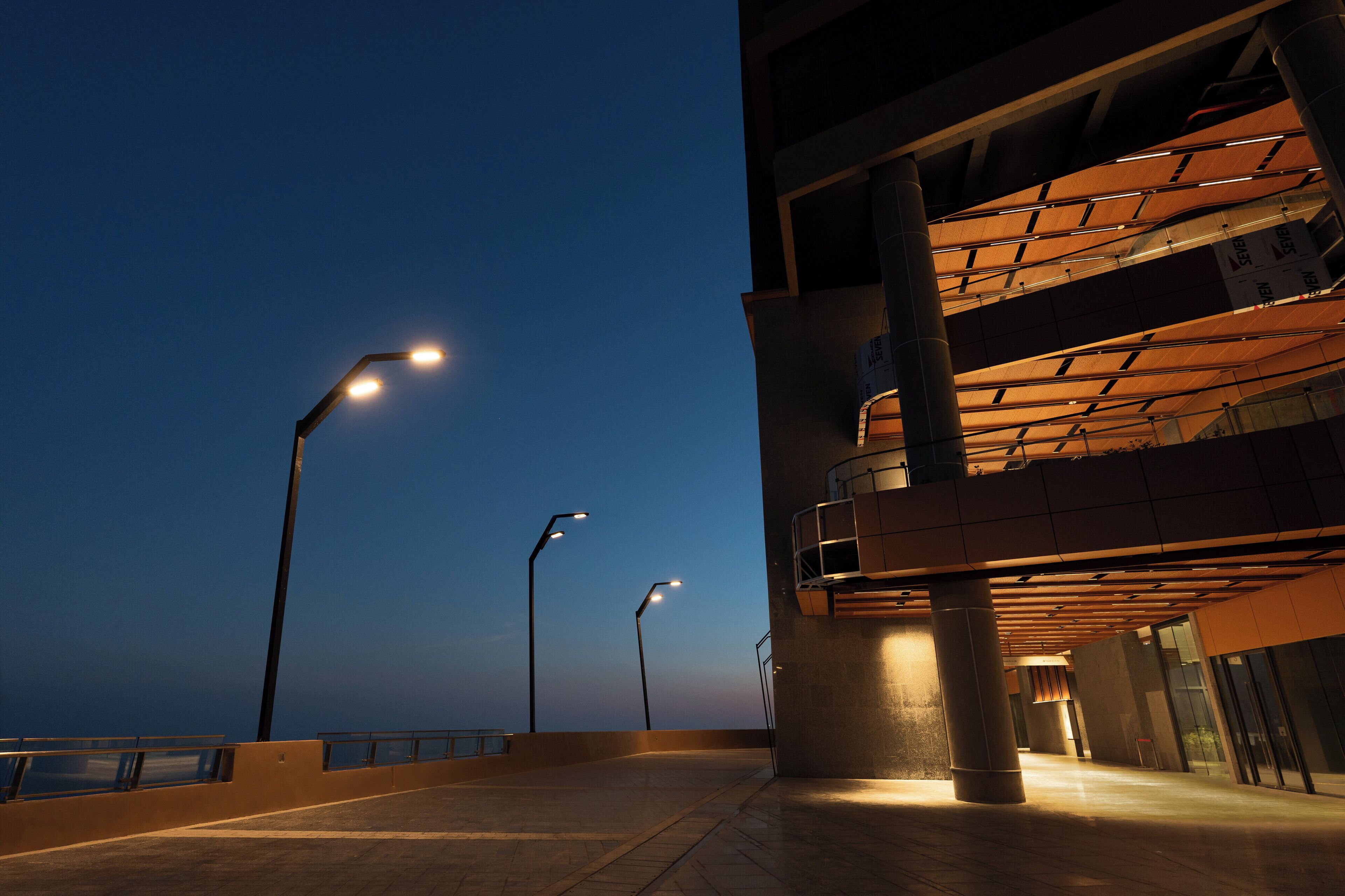 An outdoor corridor with modern architecture, featuring a curved glass facade and a series of street lamps.